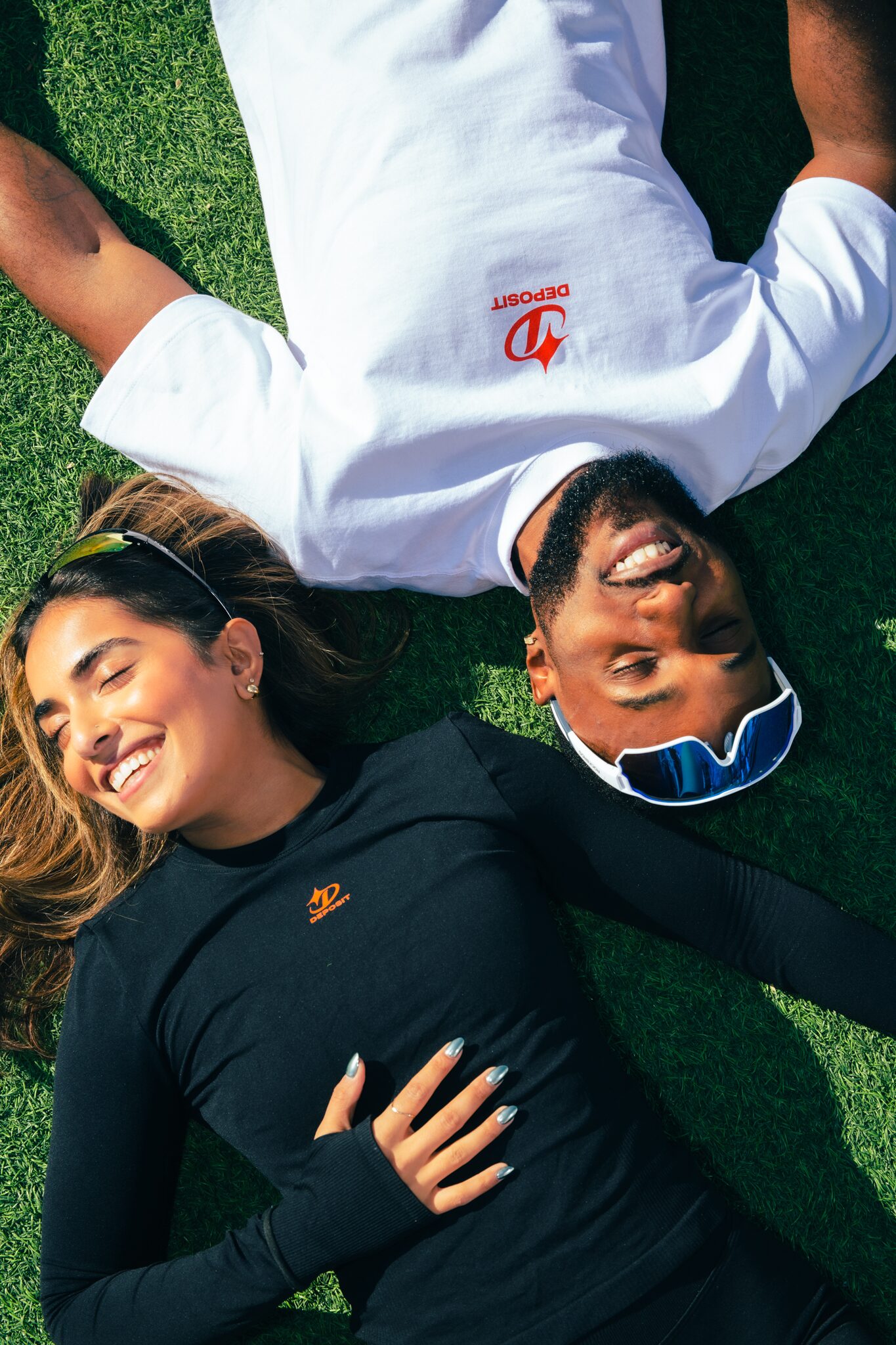 Man and woman lying on turf with heads together, smiling.